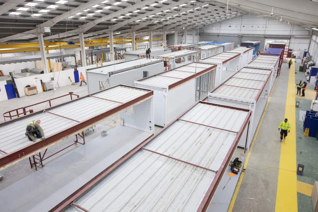 Overview of Premier Modular Offsite Construction factory. Modular units being built by construction workers wearing high-vis vests.