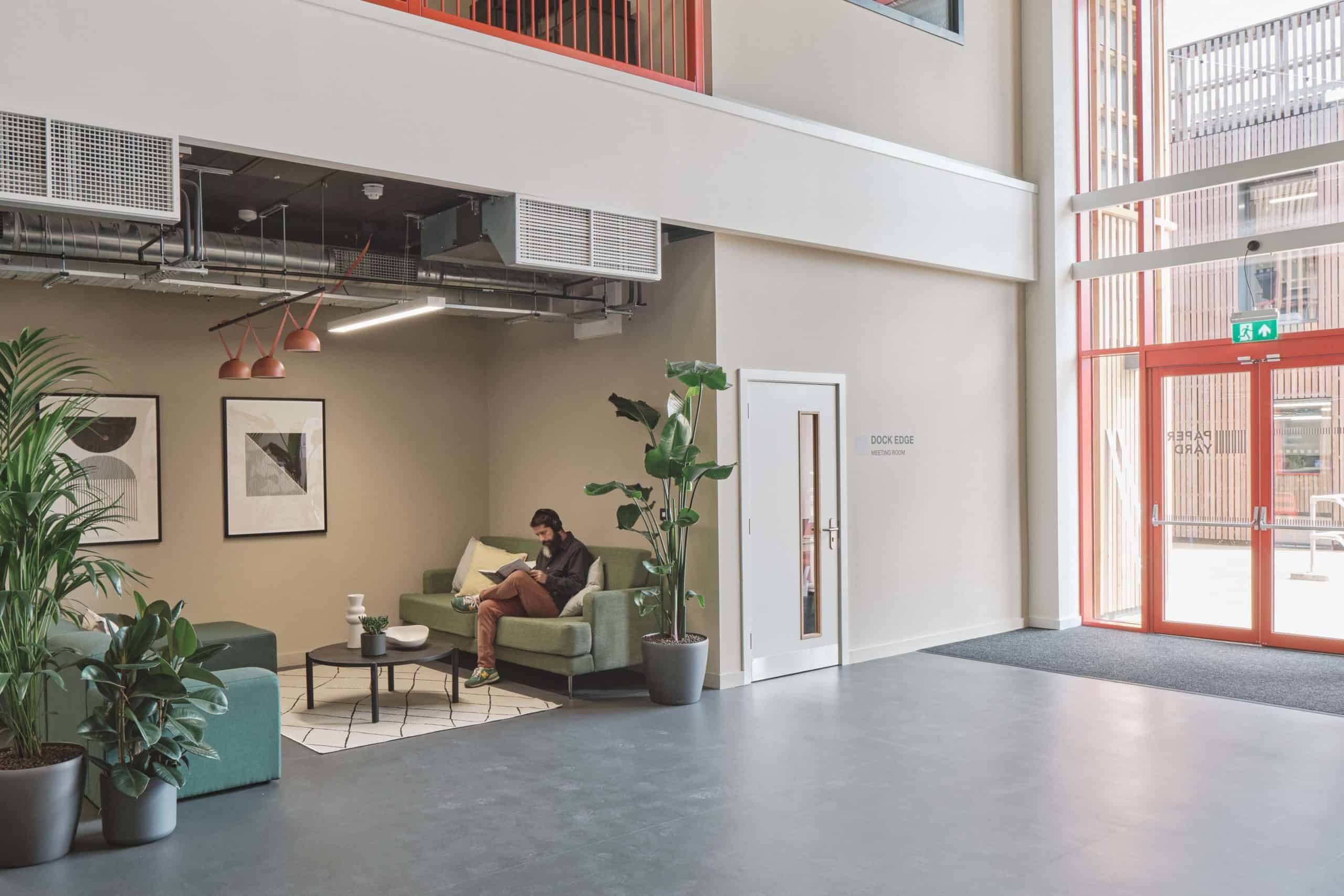 Inside the entrance of modular building, waiting area with two sofas. small coffee table, two plants either side with a man sat on the sofa.