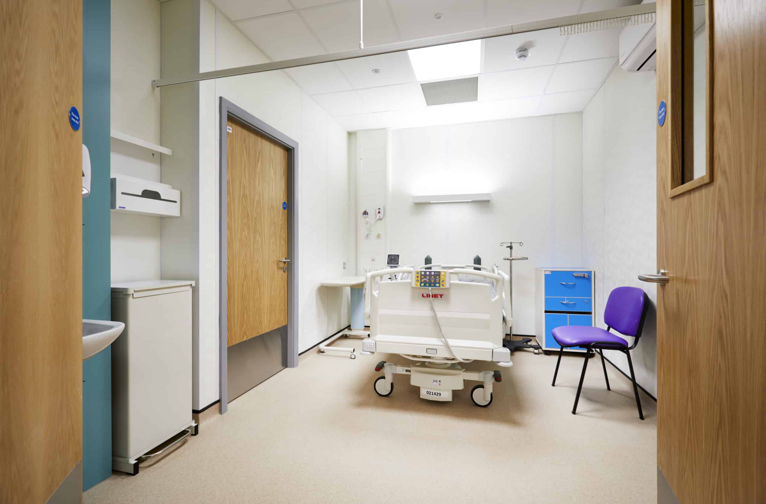 Hospital room inside a modular healthcare building. Hosptial bed, with a chair beside it and a sink.