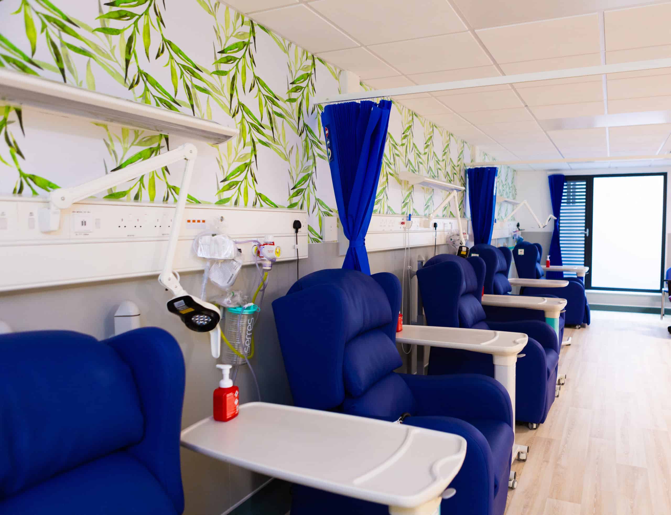 Hospital room inside modular healthcare building. Patient area, with comfy chairs and desks, as well as curtains for privacy although in this image they are pulled back.