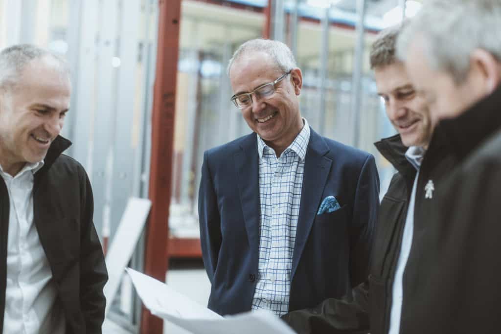 Four men who work at Premier Modular. Wearing suits, looking over plans. 