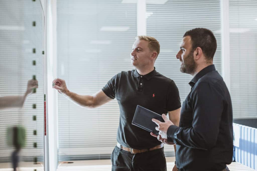 Two premier modular workers, stood discussing plans on a whiteboard. 