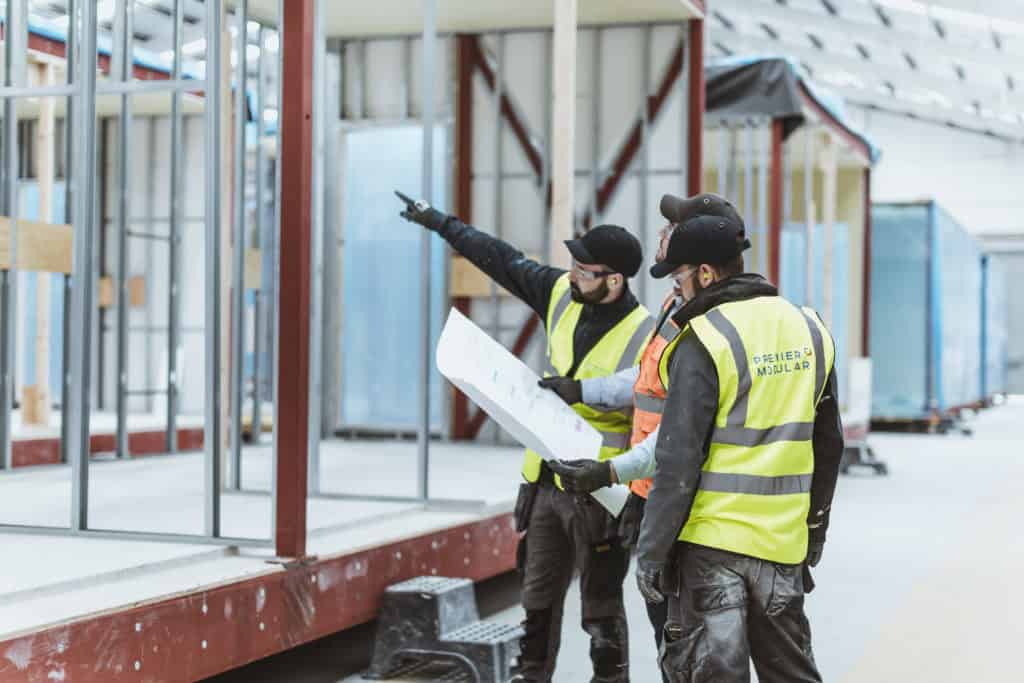 Premier Modular construction workers, pointing at a modular unit. Three workers huddled around some blue prints.